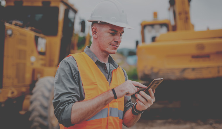 Man using mobile phone in front of construction equipment